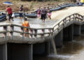 Personas cruzan un puente en mal estado en la región de San Antonio del Sur una semana después del paso de la tormenta tropical Oscar. Foto: Ernesto Mastrascusa / POOL / EFE.