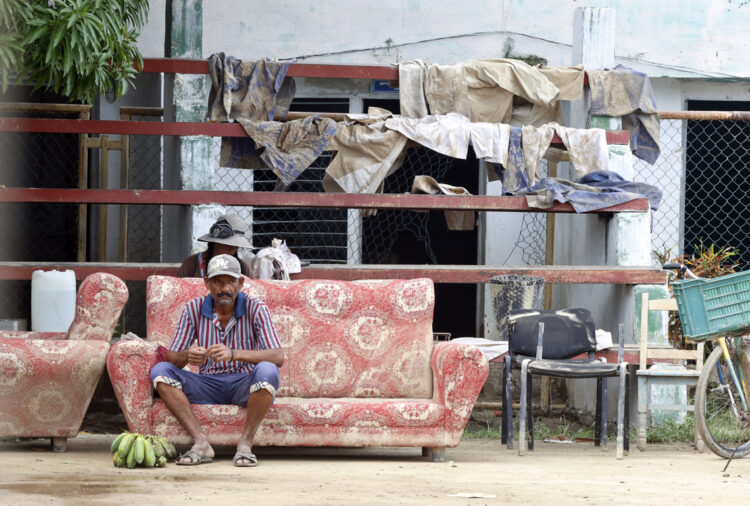 Un hombre descansa en el exterior de una vivienda en la región de San Antonio del Sur una semana después del paso de la tormenta tropical Oscar. Foto: Ernesto Mastrascusa / POOL / EFE.