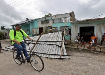 Un hombre transita en bicicleta frente a una vivienda con el techo caído tras el paso del huracán Rafael, en la provincia de Artemisa. Foto: Ernesto Mastrascusa / EFE.