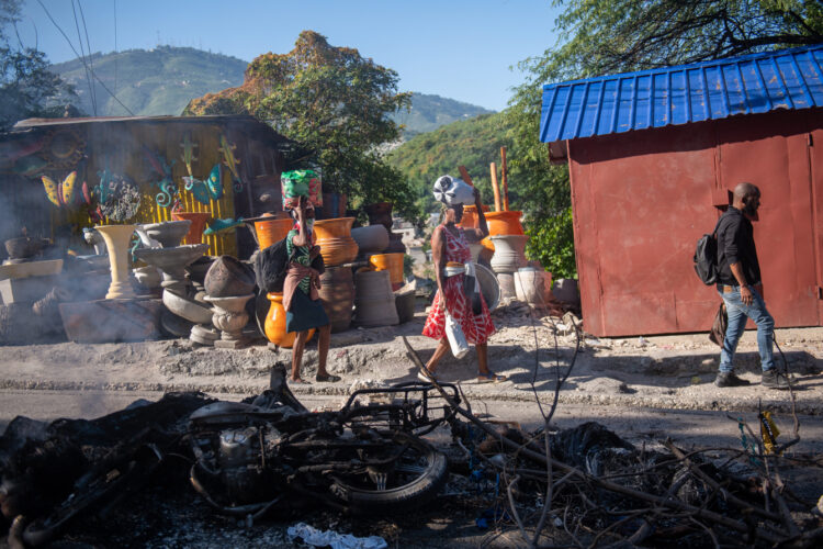 Personas pasan frente a los restos de una hoguera donde incineraron a un pandillero, en una calle de Puerto Príncipe. Foto: Johnson Sabin/EFE.