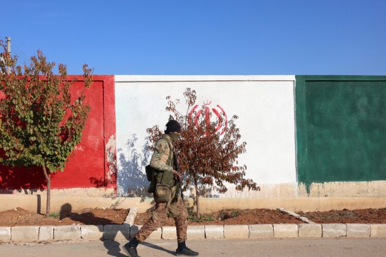 Khan Sheikhoun, 03/12/2024.- Un miembro de la oposición siria camina delante de un muro pintado con los colores de la bandera iraní en una posición militar supuestamente utilizada por las fuerzas iraníes después de que fuera capturada por la oposición siria en la ciudad de Khan Sheikhoun, en la campiña de Idlib, Siria, 03 Diciembre de 2024. Las fuerzas de oposición sirias, lideradas por el grupo militante islamista Hayat Tahrir al-Sham (HTS), lanzaron una ofensiva el 27 de noviembre, tomando gran parte de Alepo, Siria. segunda ciudad más grande. La ofensiva desencadenó contraataques de las fuerzas del régimen sirio, así como ataques aéreos rusos y sirios contra zonas controladas por la oposición. (Rusia, Siria) Foto: EFE/EPA/MOHAMMED AL RIFAI