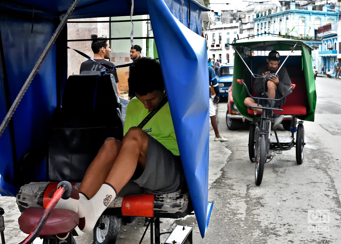 Personas en un bicitaxi revisan el móvil y se protegen del frío en La Habana. Y Foto: Otmaro Rodríguez.