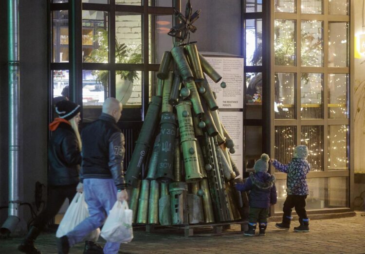 La gente pasa junto a un árbol de Navidad hecho con munición usada e instalado cerca de una cafetería en la víspera de Año Nuevo en el centro de Kiev, Ucrania, el 31 de diciembre de 2024. Foto: EFE/EPA/SERGEY DOLZHENKO.